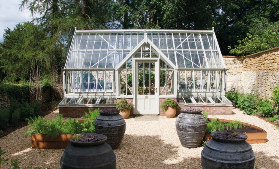 Large aluminium greenhouse with cold frames in a walled garden, surrounded by planters.