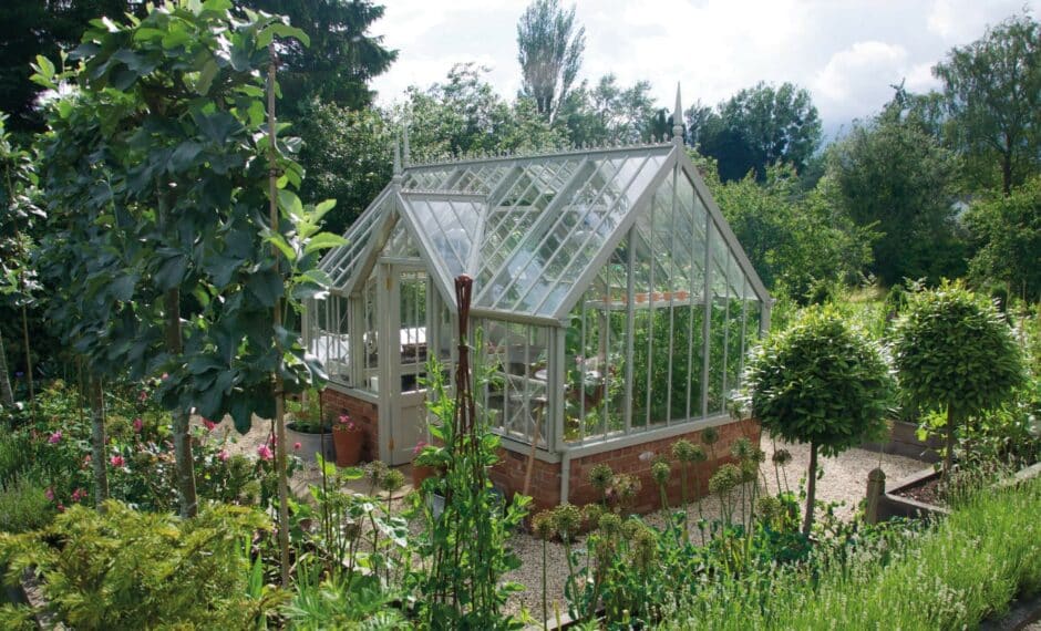 Aluminium Victorian greenhouse with a flat-fronted lobby on a brick base surrounded by green foliage.