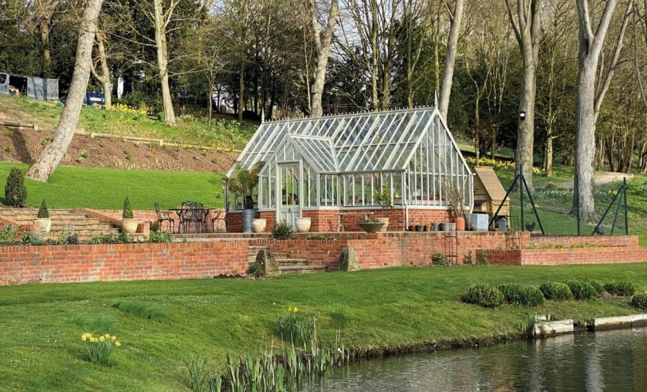 Alitex Cliveden greenhouse on a red brick base in a large hilled garden