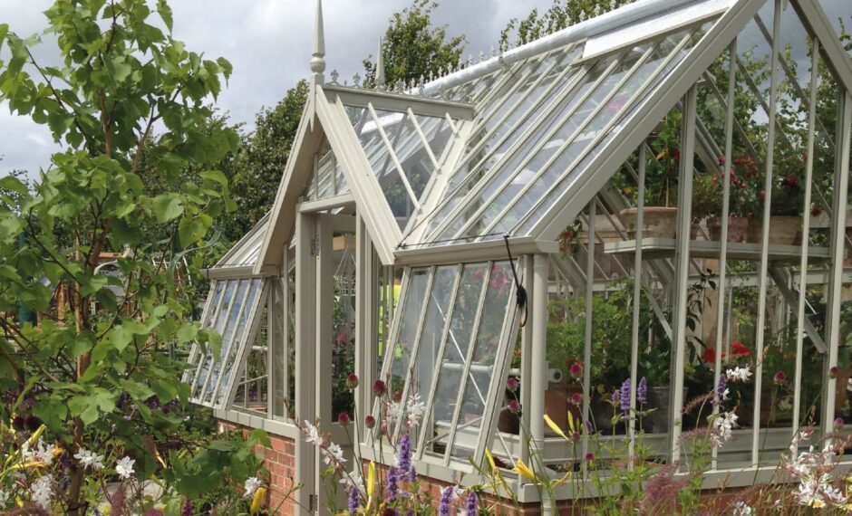 Victorian greenhouse with a flat fronted lobby and open vents surrounded by trees and plants.