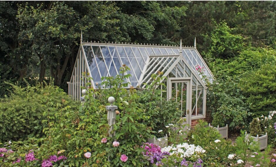 Aluminium Victorian style greenhouse with a lobby surrounded by greenery and plants.