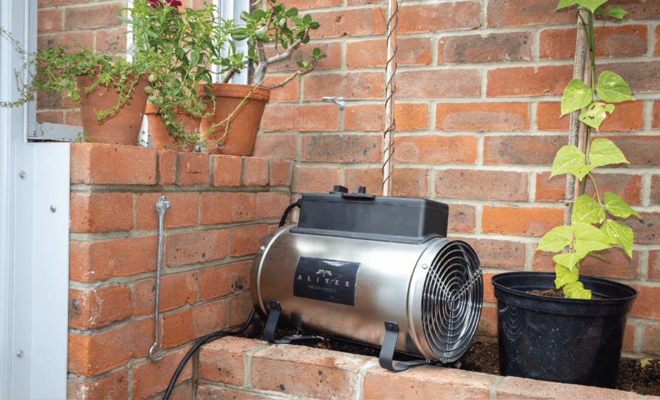 Silver Electric Greenhouse Heater on a red brick wall within a lean-to greenhouse