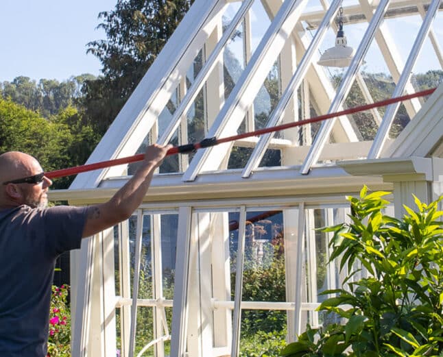 Person cleaning outside of a greenhouse with a large brush