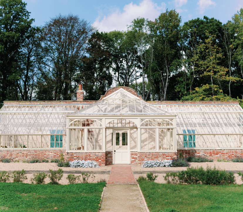 Large Bespoke Monopitch Greenhouse in white on a red brick base. In front is a stone path with grass either side.