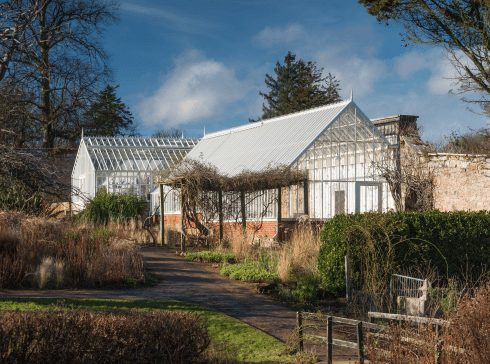 Large monopitch greenhouse on a red brick base in a walled garden.