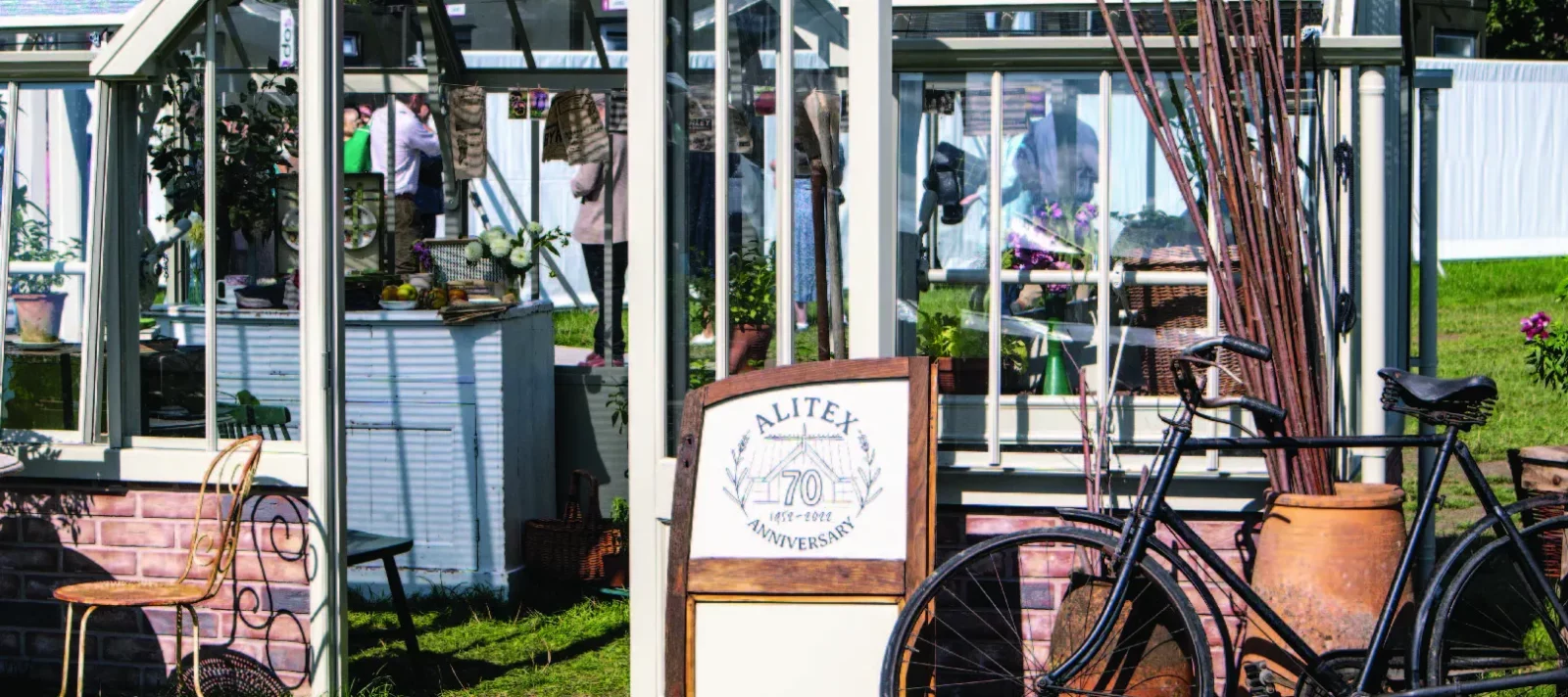 Alitex National Trust Mottisfont Greenhouse at Goodwood Revival, styled with an old vintage bike and car door at the front, with a large ceramic pot filled with sticks.