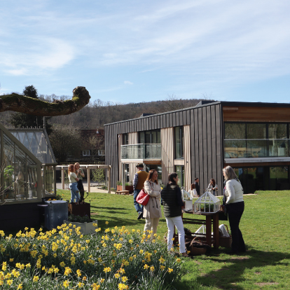Guests attend an open morning onsite at Alitex which is located in South Harting in Hampshire. The image displays the guests in conversation with Alitex staff amongst some vibrant plants and an Alitex greenhouse.
